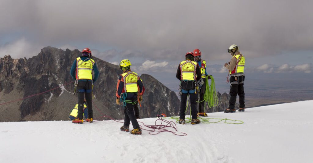 Group of mountain rescuers in safety vests and helmets preparing ropes in snowy terrain.